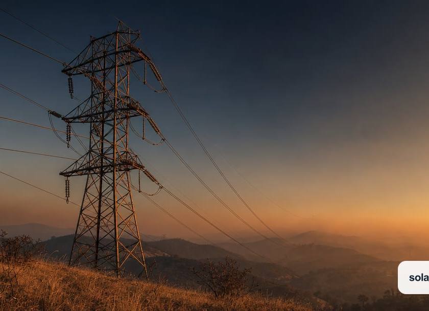 A weathered high-voltage transmission tower and sagging power lines standing alone against a smoke-tinged California dusk sky, distant dry…